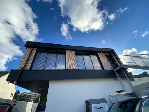 Maison moderne à deux étages avec fenêtres larges et balustrade en acier. Ciel bleu en arrière-plan.